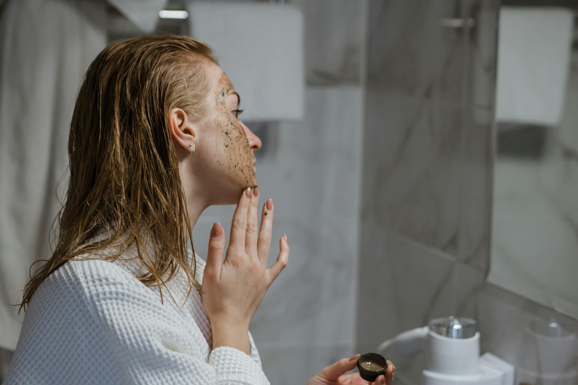 Kobieta w nowoczesnej łazience nakłada kawowy peeling na twarz