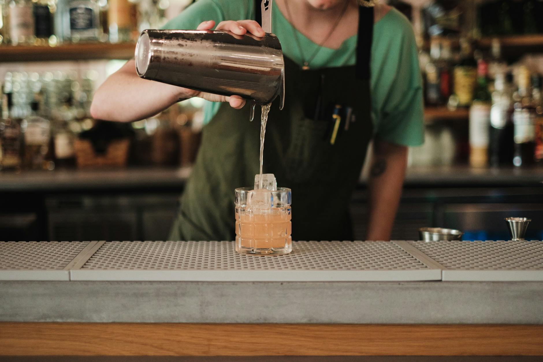 Barman przelewa kolorowego drinka do szkła przy eleganckim barze