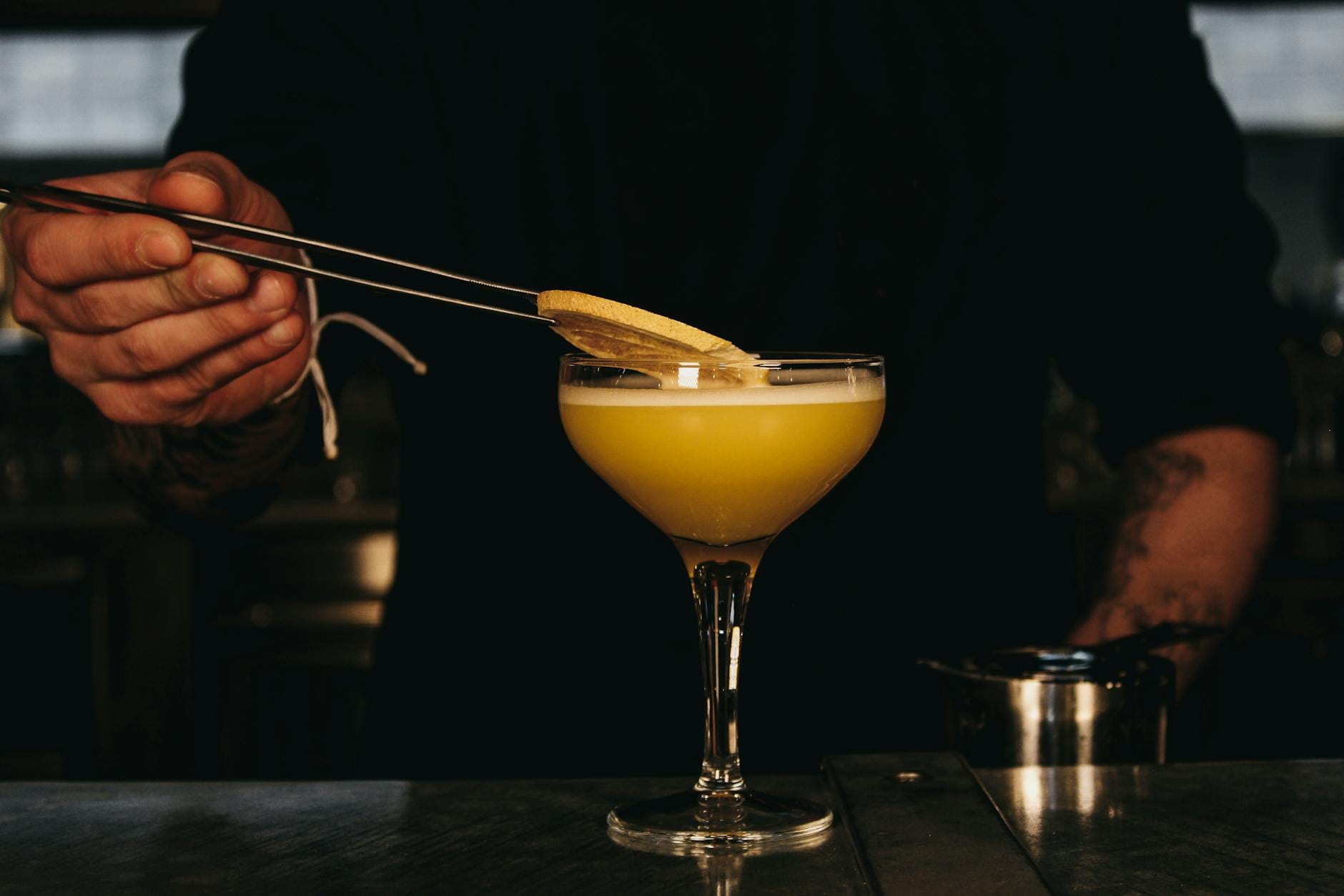 Barman szczypcami dekoruje cytrusowego drinka plastrem cytryny