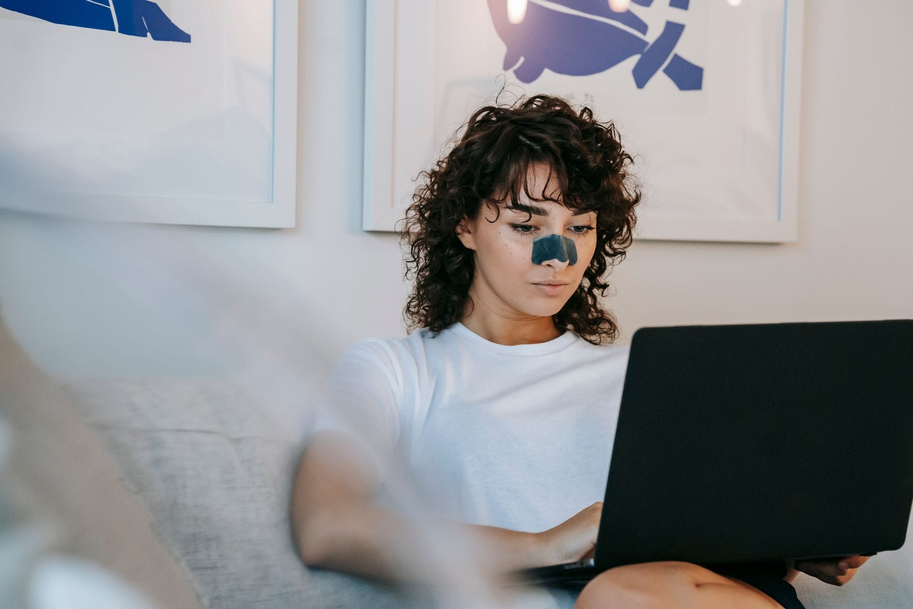 Młoda kobieta z plastrem na nosie pracuje na laptopie w mieszkaniu