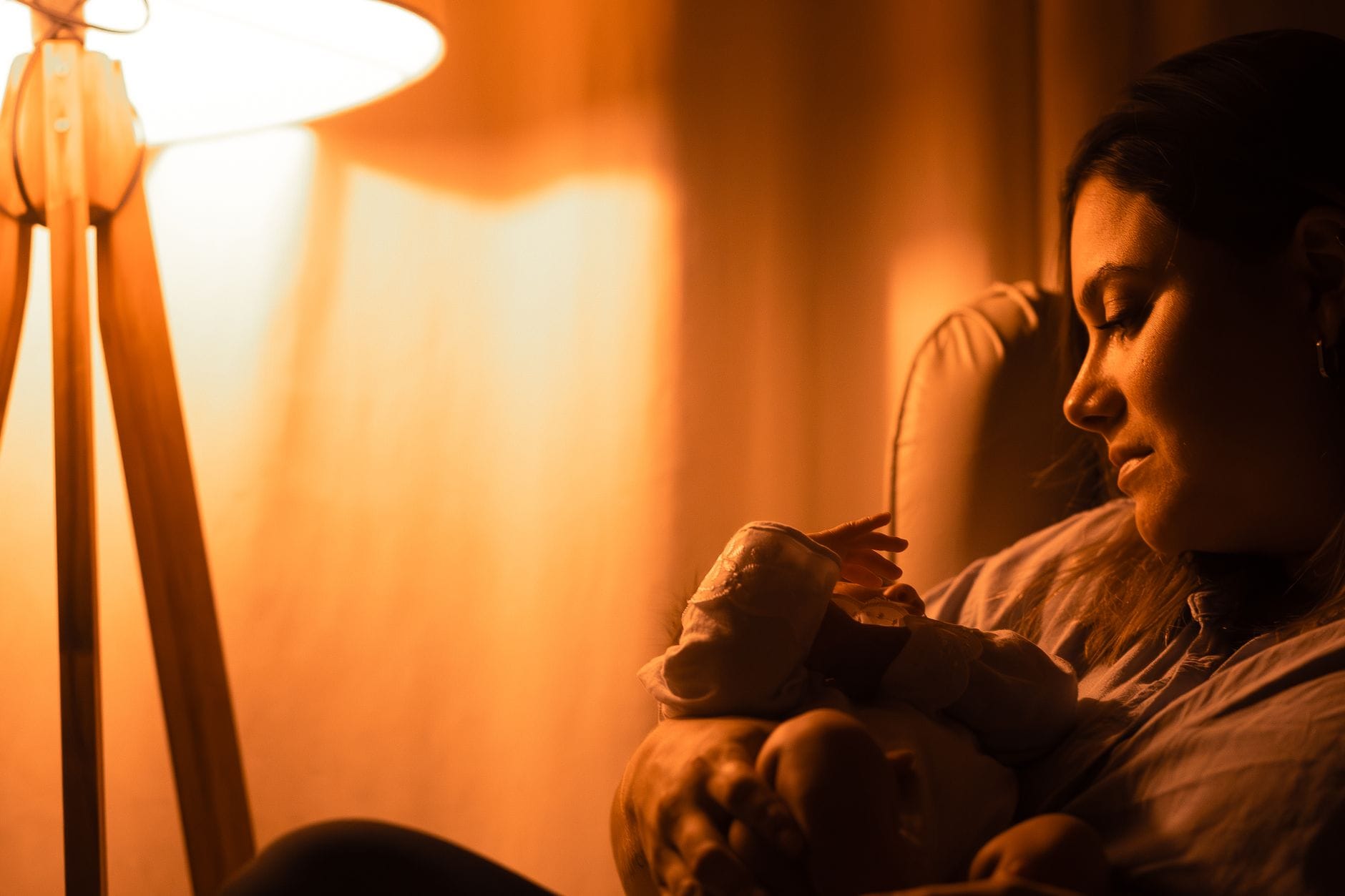 Mama patrzy czule na śpiące niemowlę w ciepłym świetle lampki