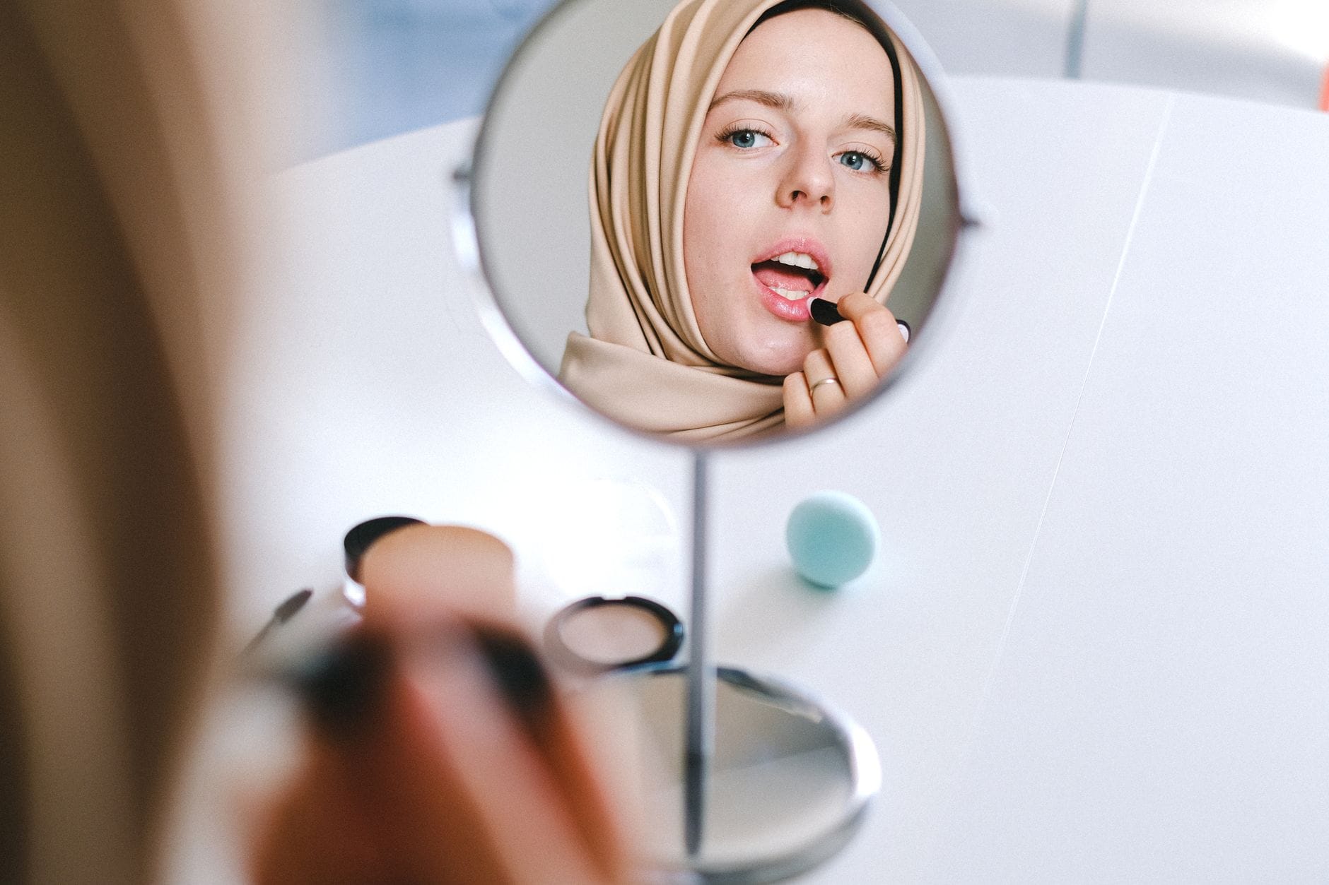 Muzułmanka w hijabie nakłada pomadkę, patrząc w lustro